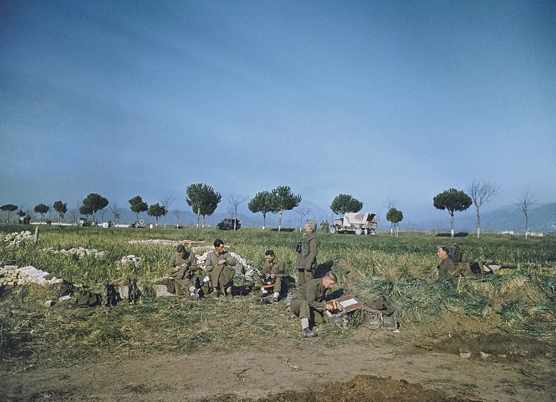 A Royal Artillery Bofors gun crew making repairs to their uniforms durung operations to cross the Garigliano river in Italy, 19 January 1944 doing some sewing. Transport on the Via Appia can be seen in the background. TR1527